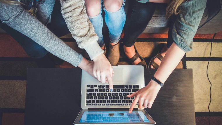 Draufsicht auf mehrere Hände, die gemeinsam an einem Laptop arbeiten