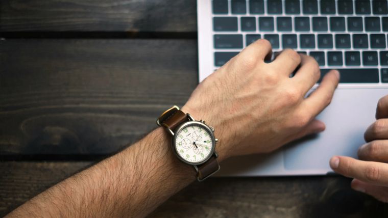 Unterarm mit Armbanduhr an einem Laptop auf dunklem Holztisch